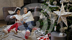 Portrait of African American mom and her little daughter playing the game with joysticks and rejoicing. Woman and girl