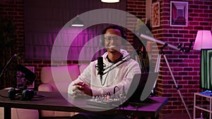 Portrait of african american online radio host sitting at desk in home recording studio with boom arm microphone