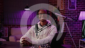 Portrait of african american online radio host sitting at desk in home recording studio with boom arm microphone