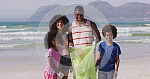 Portrait of african american parents with their children collecting rubbish and bottles from beach