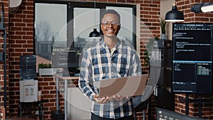 Portrait of african american programer standing working on laptop looking up and smiling