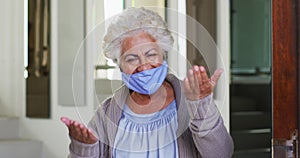 Portrait of african american senior woman wearing face mask opening front door and welcoming at home