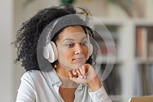 Portrait of African American woman listening to information or music in large white wireless headphones. Brunette sits