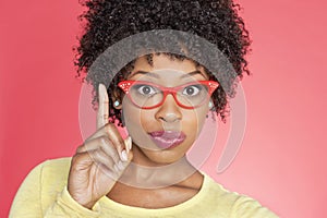 Portrait of an African American woman in retro glasses pointing upward over colored background