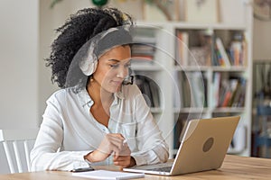 Portrait of African American woman talking on video conference call using laptop and headphones taking notes on notepad