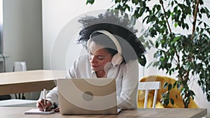 Portrait of African American woman talking on video conference call using laptop and headphones taking notes on notepad
