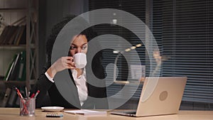 Portrait of African American woman typing on laptop and drinking coffee. Manager replies to email to the customer