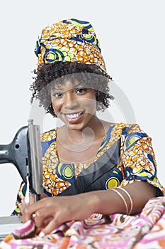 Portrait of an African American woman using sewing machine over gray background