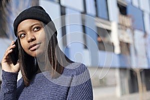 Portrait of African American young beautiful woman wearing a wool cap standing on the street while using a mobile phone