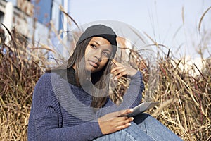 Portrait of African American young beautiful woman wearing a wool cap standing on the street while using a mobile phone