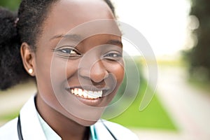 Portrait of an African American young girl. Doctor in a white coat, with a phonendoscope, smile, outdoors