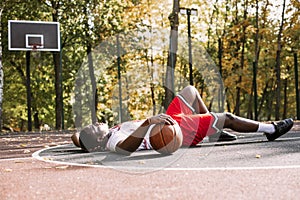 Portrait of an African American young man holding a basketball and sitting on a basketball court. Take a break during