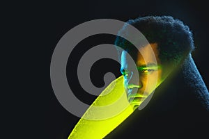 Portrait of African-American young man in neon yellow glow on dark background.