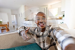 Portrait of african american young man pointing and looking at camera while sitting in living room