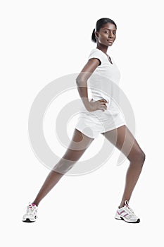 Portrait of an African American young woman stretching legs against white background