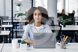 Portrait of african american young woman working in coworking office after quarantine. Friendly lady sitting at computer