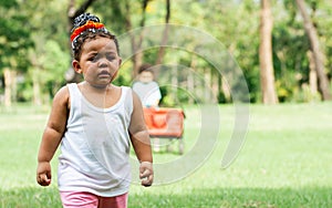 Portrait of African black adorable little girl crying with sadness while standing and playing in outdoor backyard, green field,