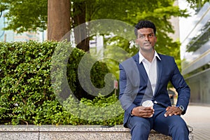 Portrait of African businessman holding take away coffee cup outdoors in city while sitting