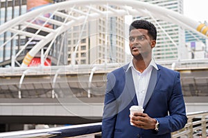 Portrait of African businessman outdoors thinking and holding take away coffee cup