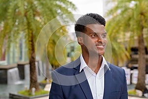 Portrait of African businessman smiling and thinking outdoors in city during summer