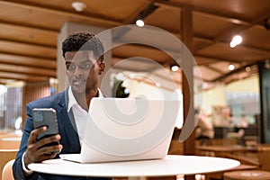 Portrait of African businessman using laptop computer and mobile phone in coffee shop