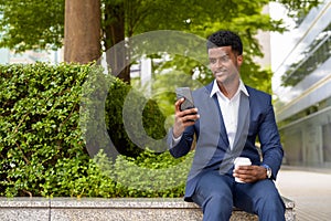 Portrait of African businessman using phone and holding take away coffee cup outdoors in city