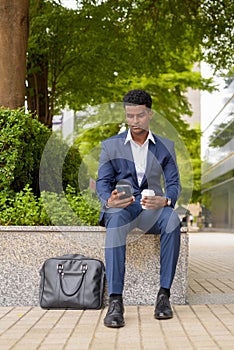 Portrait of African businessman using phone and holding take away coffee cup outdoors in city while using mobile phone