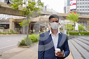 Portrait of African businessman wearing face mask outdoors and holding take away coffee cup