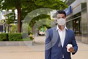 Portrait of African businessman wearing face mask outdoors and holding take away coffee cup