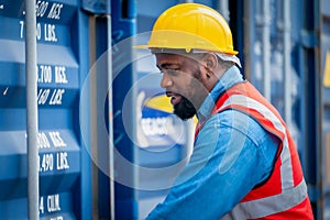 Portrait of African Engineer or foreman wears PPE checking container storage with cargo container background at sunset. Logistics