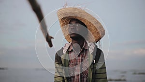 Portrait of African fisherman in straw hat. Young man sitting in boat and catches fish alone.