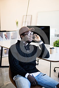 Portrait of african male executive making phone call while sitting in office. Young businessman talking on mobile phone