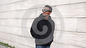 Portrait african man in black hoodie, sunglasses walking on city street looking away