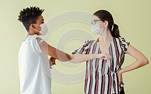 Portrait African man and Caucasian young woman making elbow bump or hit, wearing face masks, getting vaccination to protect virus