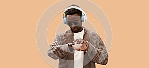 Portrait of african man listening to music in headphones looking at smart watch using voice assistant or takes calling isolated on