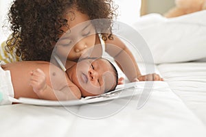 Portrait of African newborn baby boy in diaper on a white bed was kissed by his little sister