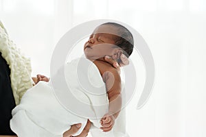 Portrait of African newborn baby boy wrapped in a blanket sleeping on motherâ€™s hands on white background