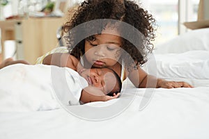 Portrait of African newborn baby sleeping on a white bed. His little sister kissing infant boy with love. New siblings relationshi