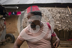 Portrait of An African Older Man in Red Muslim Taqiyyah Fez Hat posing with a stick for lame people on Yard Near the