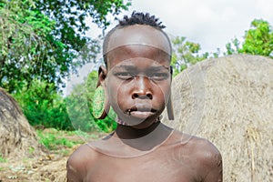 Portrait of African Teenager with a big traditional wooden earrings in the local Mursi tribe village