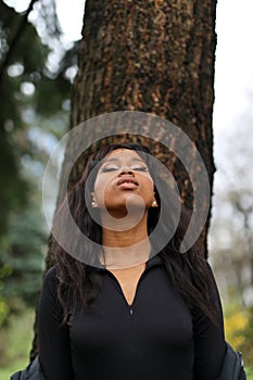 Portrait of an African woman leaning on a tree looks up, environment