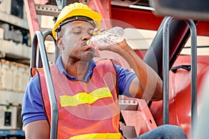 Portrait of African worker man drink water from bottle and stay on big crane truck in cargo shipping area