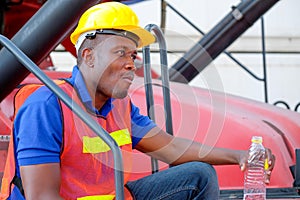 Portrait of African worker man drink water from bottle and stay on big crane truck in cargo shipping area