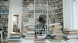 Portrait of african young man in glasses reading book while sitting in the library.