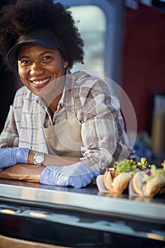 Portrait of afro-american female employee in fast food service, looking at camera, smiling,  leaned wit hands crossed, wearing