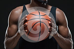 Portrait of afro american male basketball player playing with a ball over black background. Fit young man in sportswear