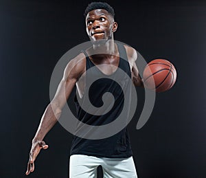 Portrait of afro american male basketball player playing with a ball over black background. Fit young man in sportswear