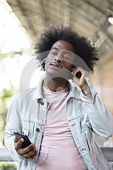 Portrait of afro american man with casual clothes and afro hairstyle enjoying music from his smart phone