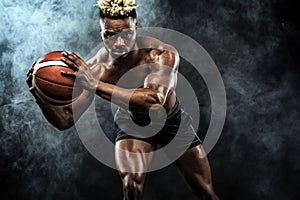 Portrait of afro-american sportsman, basketball player with a ball over black background. Fit young man in sportswear