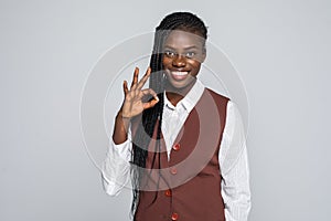 Portrait of afro american woman with white smile gesturing ok sign with fingers looking at camera isolated on grey background